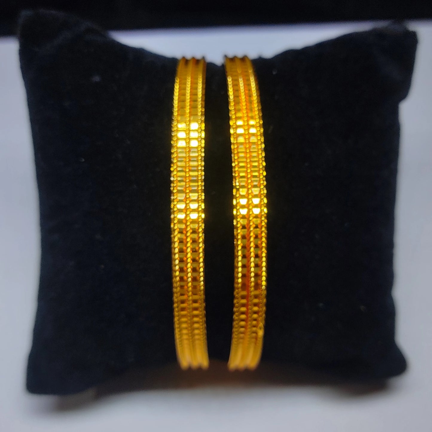 Two gold plated bangles on a black cushion