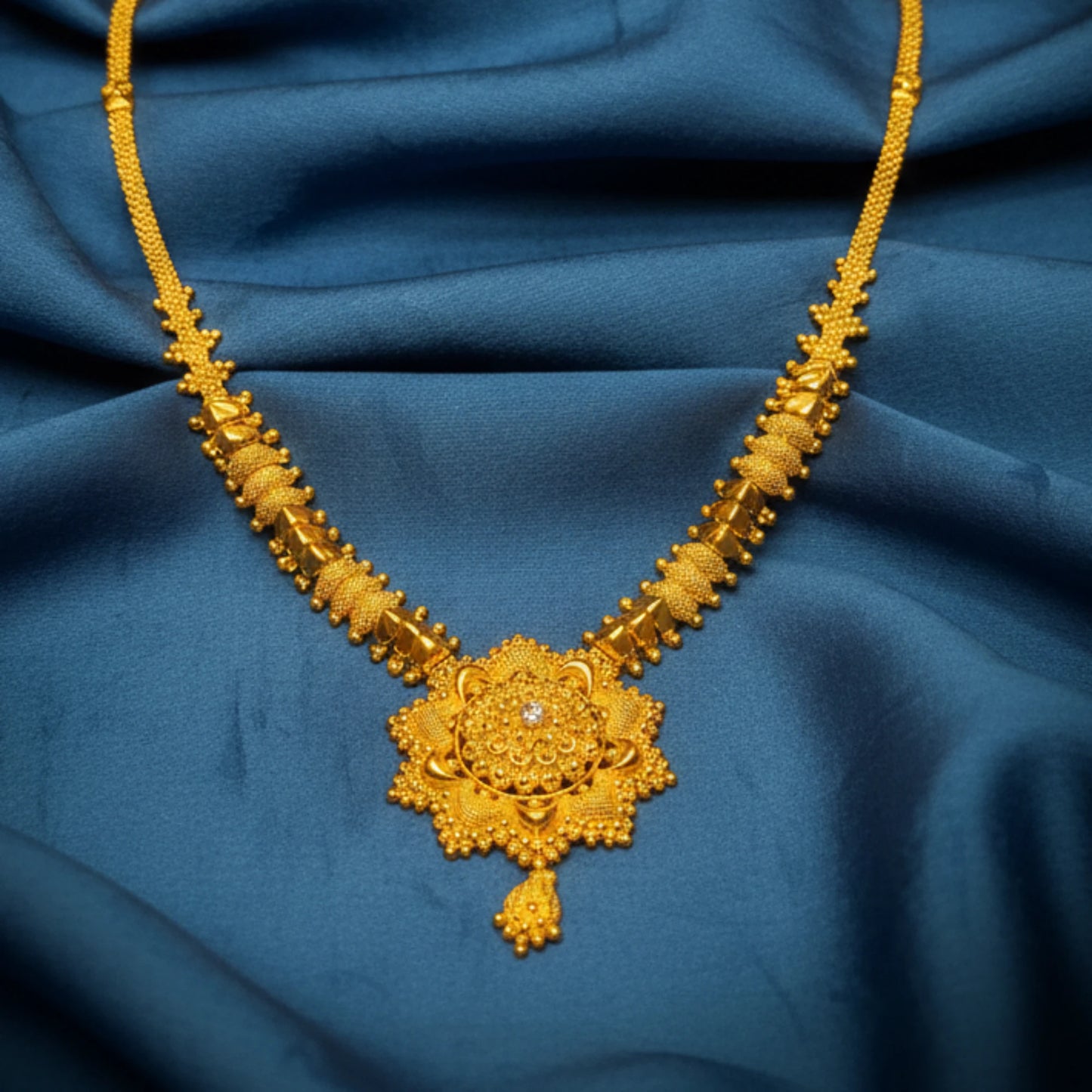 Gold plated necklace with intricate design and a floral mandala pendant on a blue fabric background