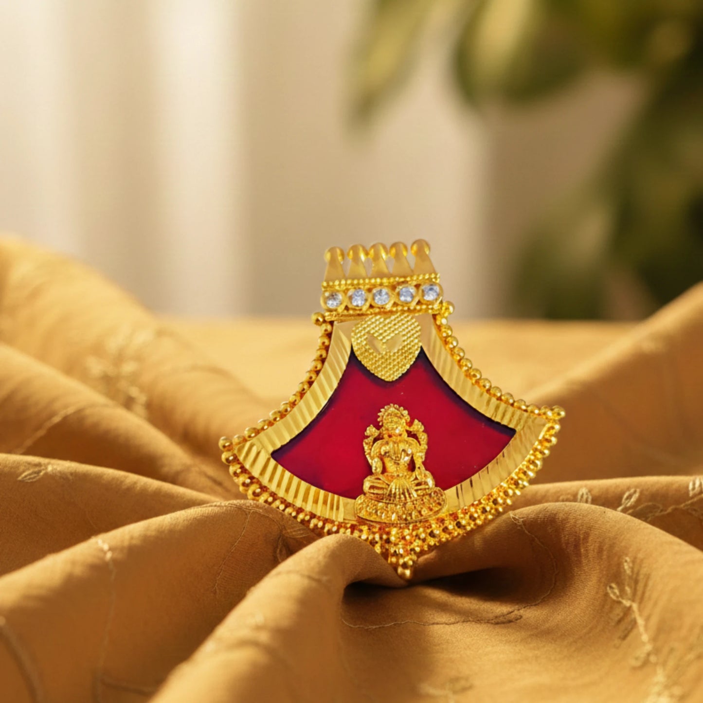 Decorative gold plated Lakshmi Pendant with red brooch on a textured fabric background