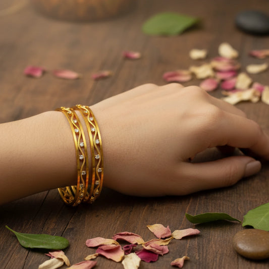 Hand wearing gold plated bangles on a wooden surface with dried petals and leaves