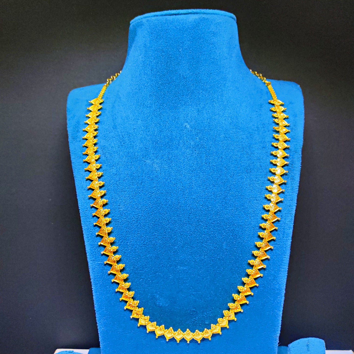 Gold plated necklace on a blue mannequin bust against a black background