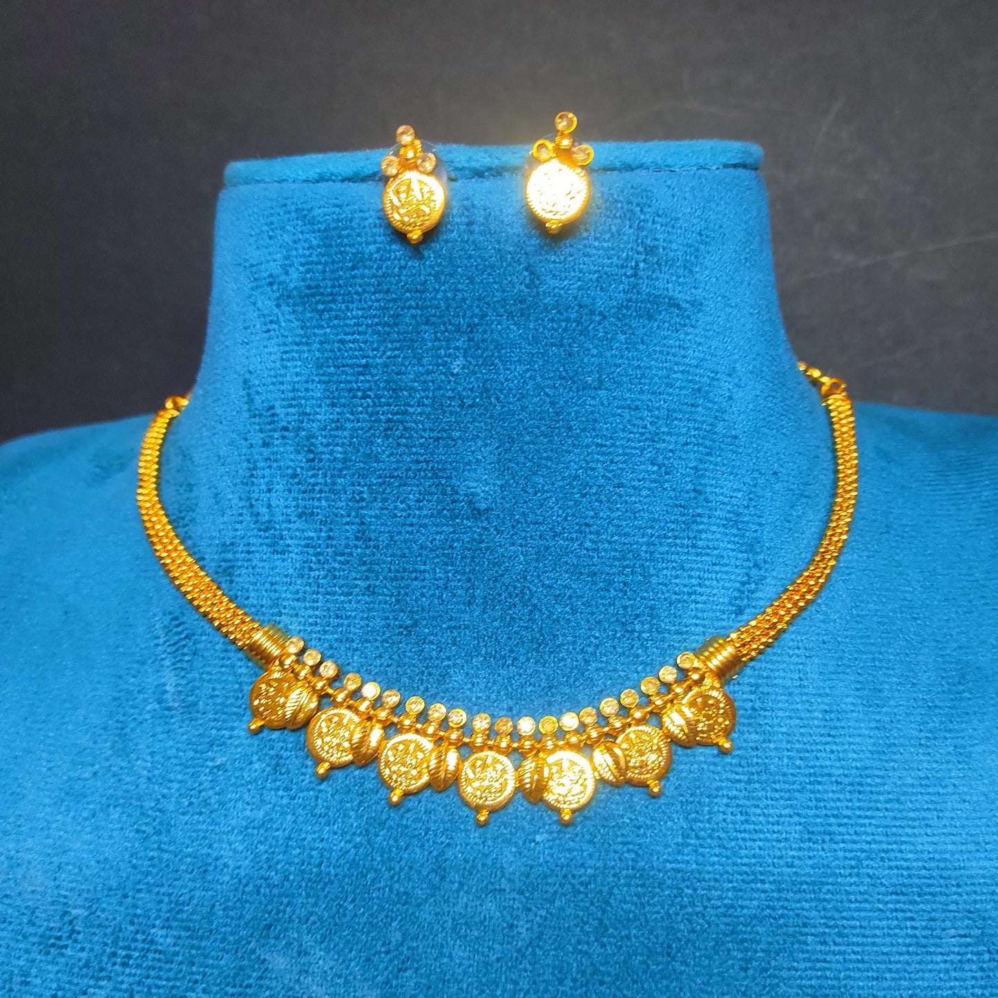 Gold toned choker necklace and earrings on a blue velvet stand against a dark background