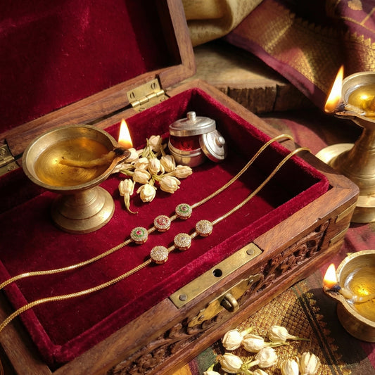 Decorative setting with Mugappu Chain on a red velvet surface, candles, and other objects.