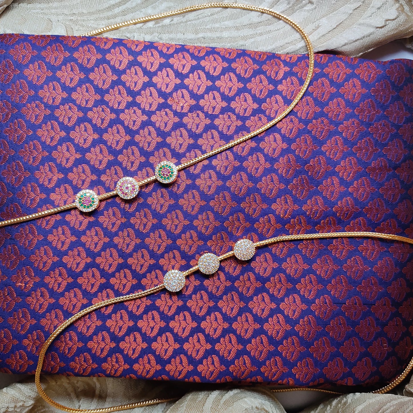 Gold toned Mugappu Chains with decorative elements on a purple fabric background
