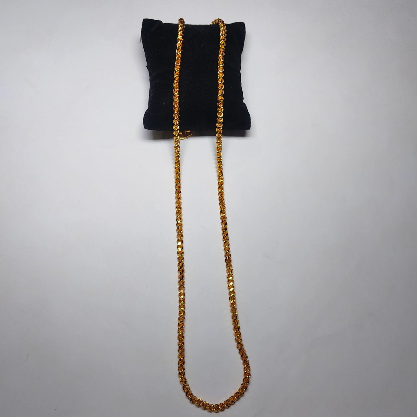 Gold plated neckchain in rope pattern on a black cushion background