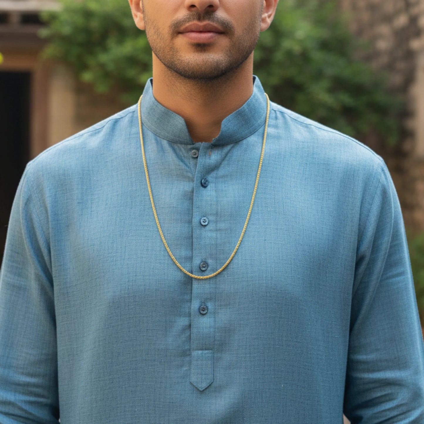 Man wearing a blue kurta with a gold plated neck chain with rope pattern and a blurred background