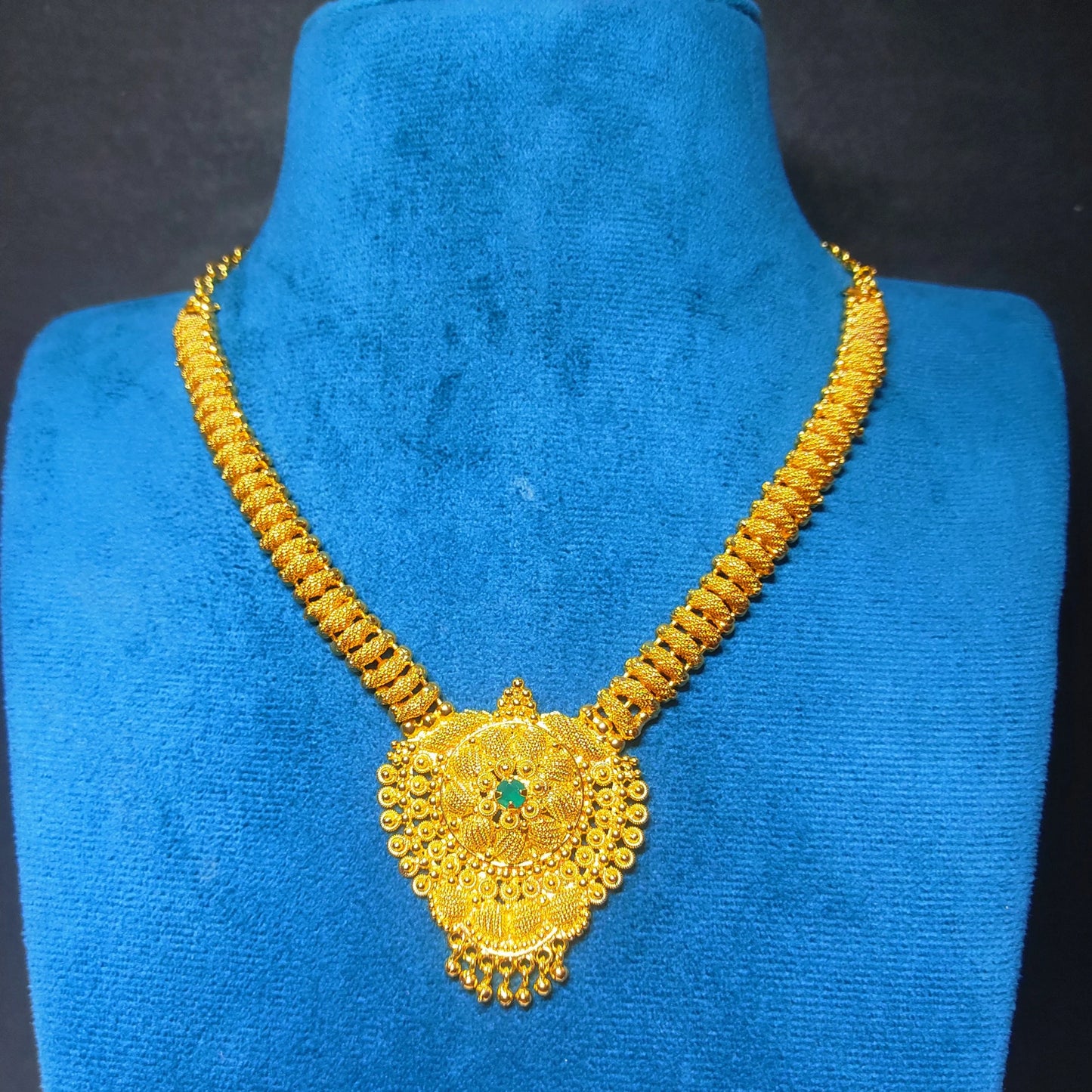 Gold plated necklace with a floral shaped mandala pendant on a blue mannequin