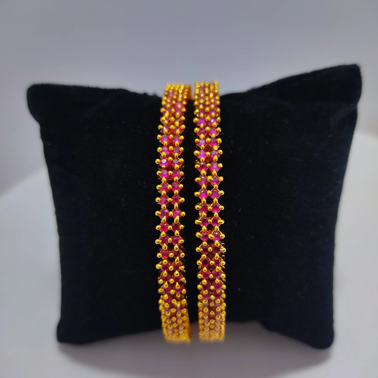 Pair of gold plated pink beaded bangles on a black cushion