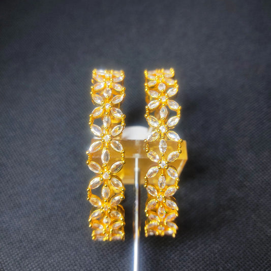 Gold toned set of bangles in floral design with clear stones on a dark background
