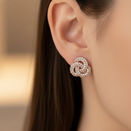 Close-up of a woman wearing a pair of rose gold earrings with rose knot design with a blurred background