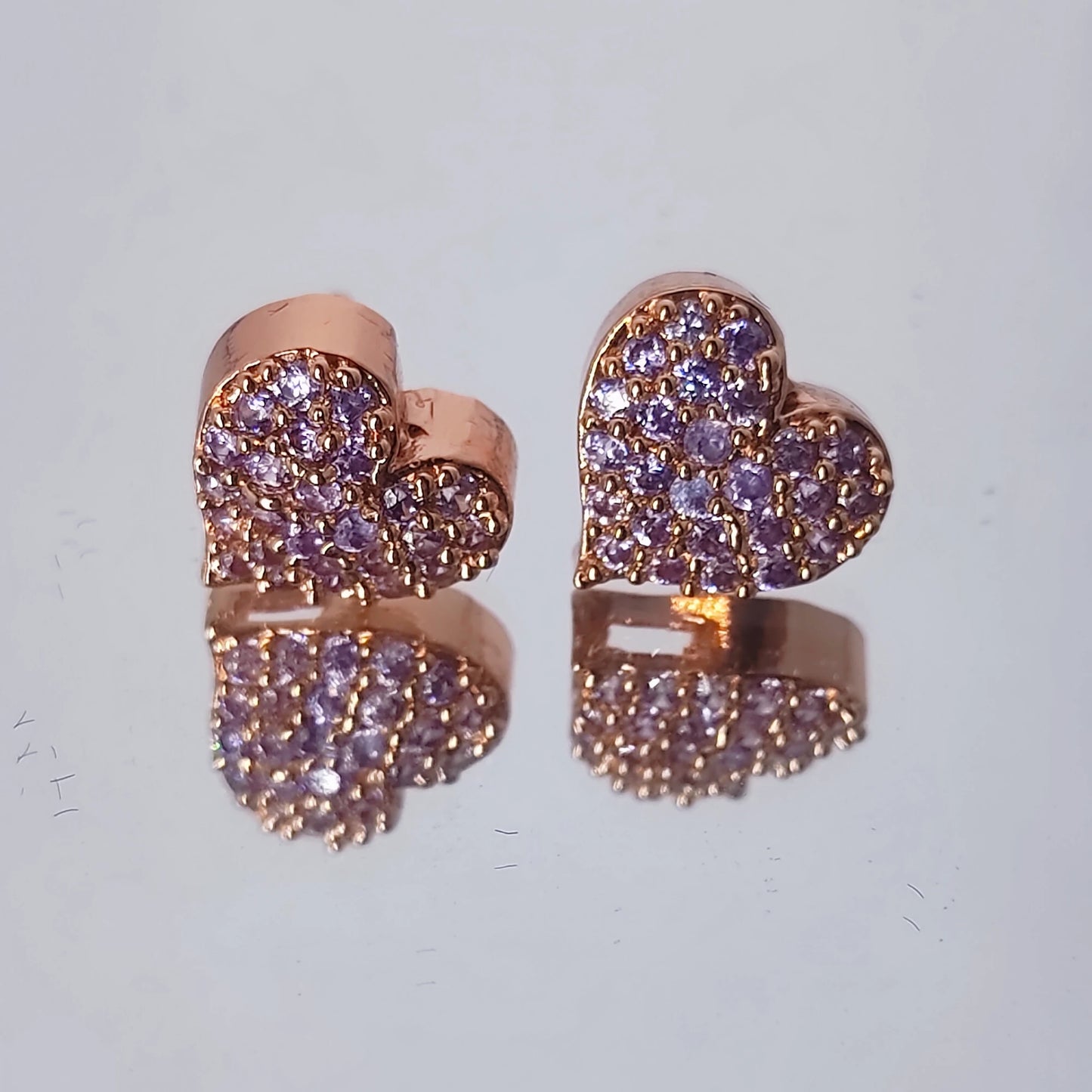 Rose gold earrings in heart shape with lavender hue stones on a mirror