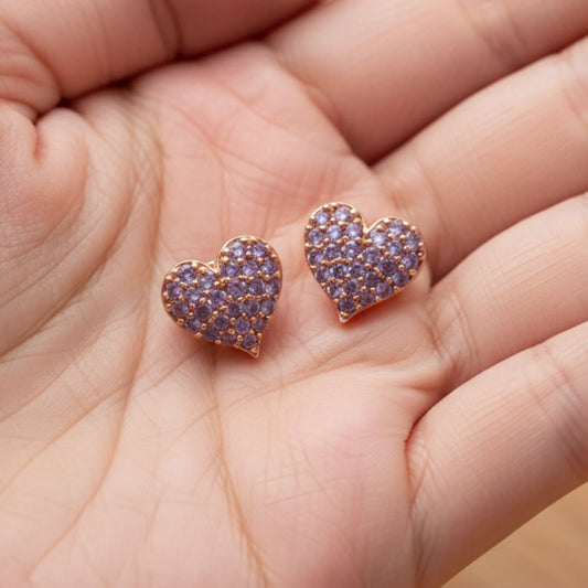 Heart-shaped earrings in rosegold with lavener hue stones held in a hand