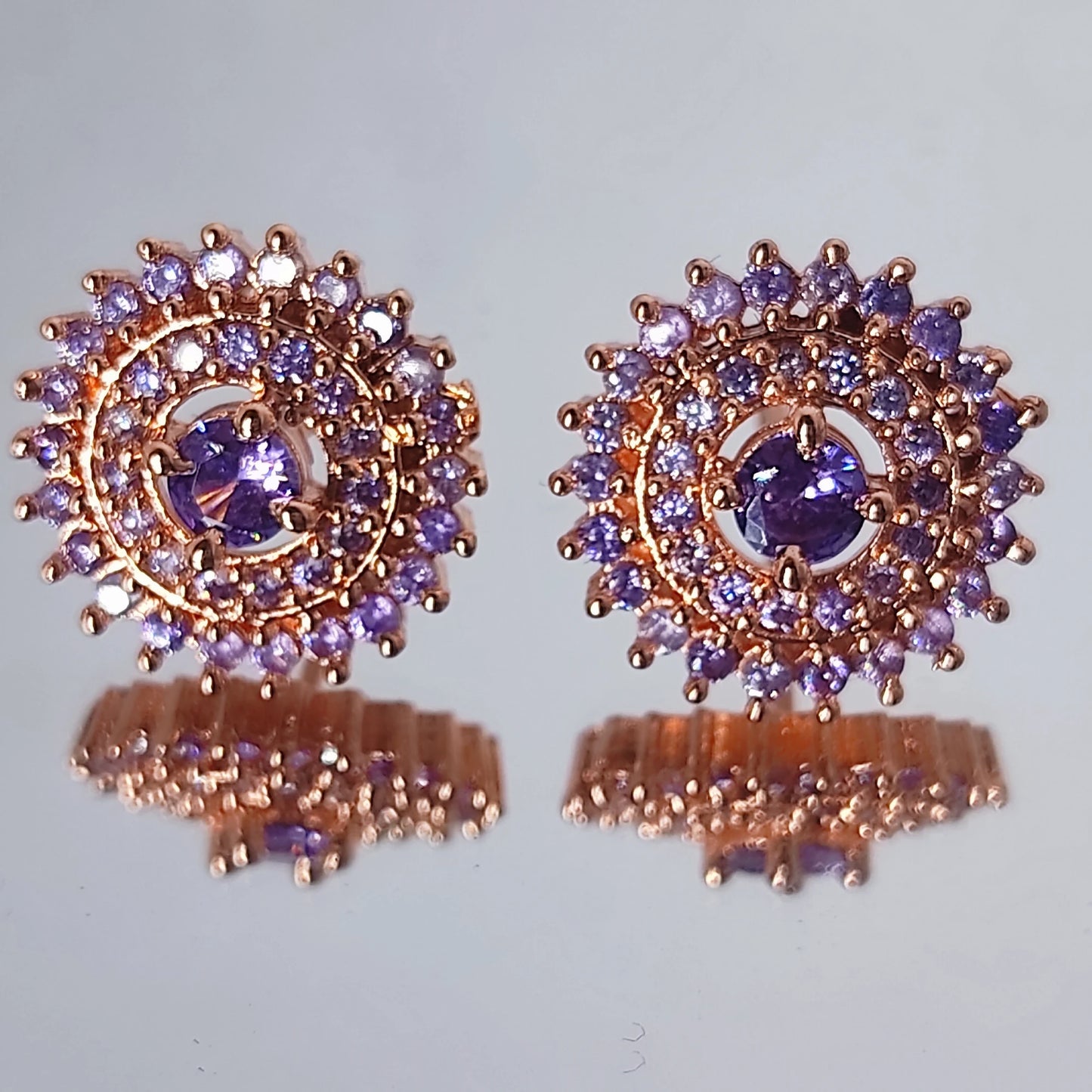 Pair of rose gold earrings with purple gemstones on a reflective surface.