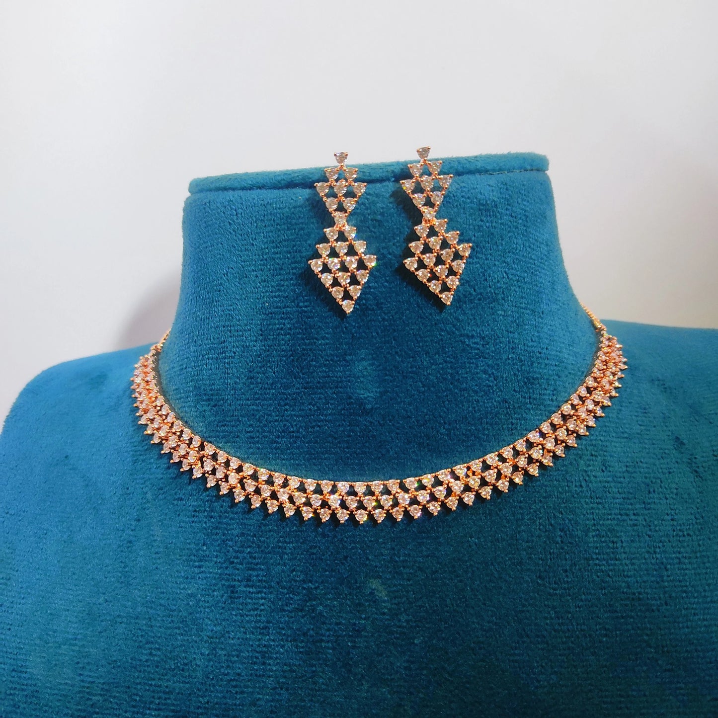 Rose gold necklace and earrings on a blue mannequin bust against a white background