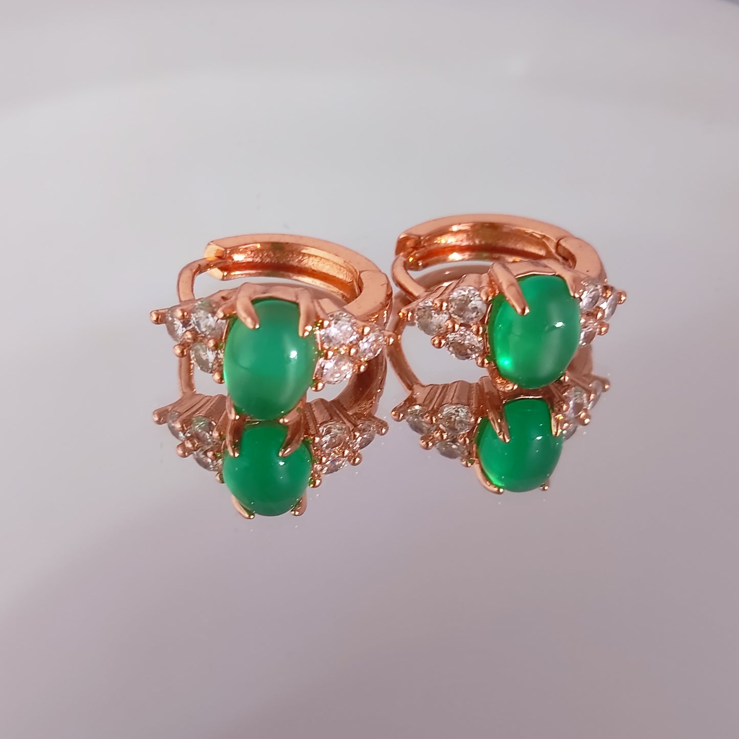 Rose gold earring with green gemstones on a gray background