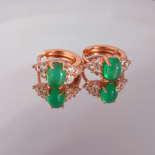 Rose gold earring with green gemstones on a gray background