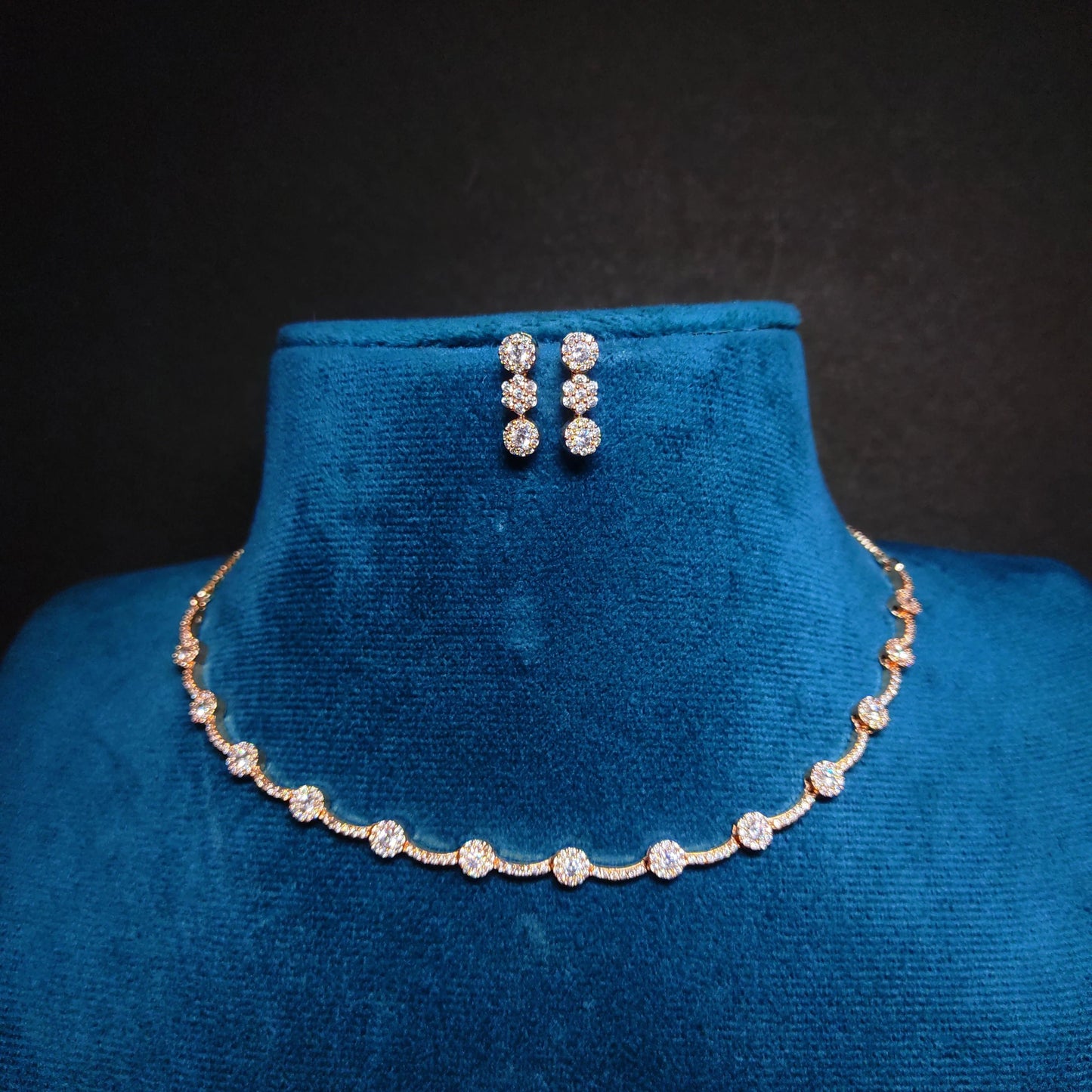 Rose Gold Jewelry set with necklace and earrings on a blue velvet stand against a black background