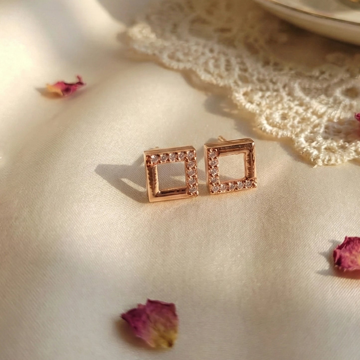 Rose gold square earrings on a textured surface with dried flowers