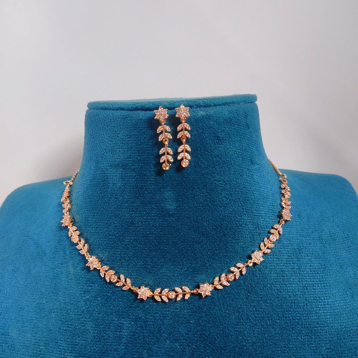 Rose gold necklace and earrings on a blue velvet stand with a grey background