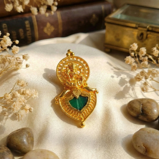 Gold plated pendant with green palakka on a textured surface with dried flowers and stones
