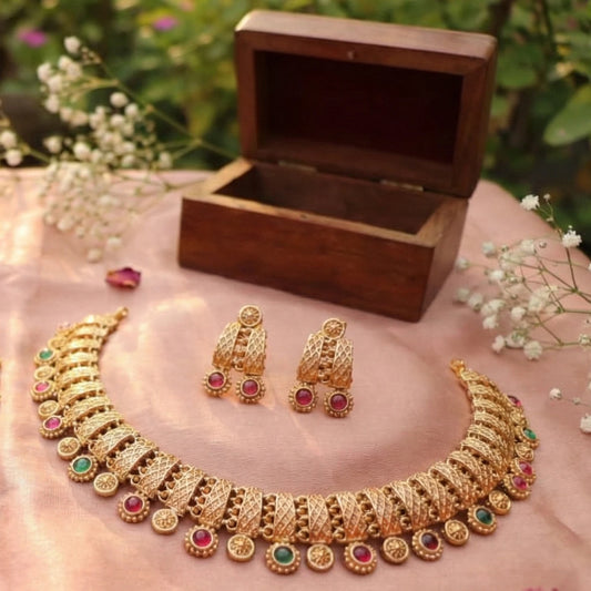 Antique Gold finish necklace and earrings set with a wooden box on a pink surface with flowers in the background