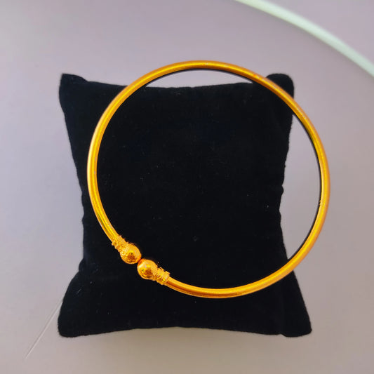 Gold plated bracelet on a black cushion with a white background