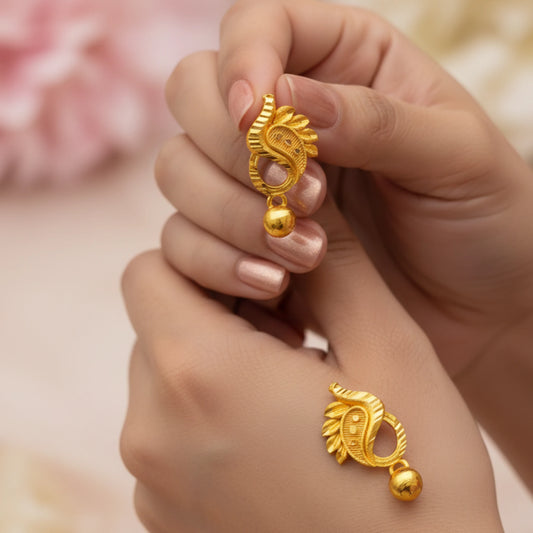 Gold plated manga mani earrings held between fingers with a soft background