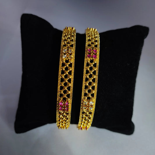Gold plated Bangles with pink stones on a black cushion against a grey background