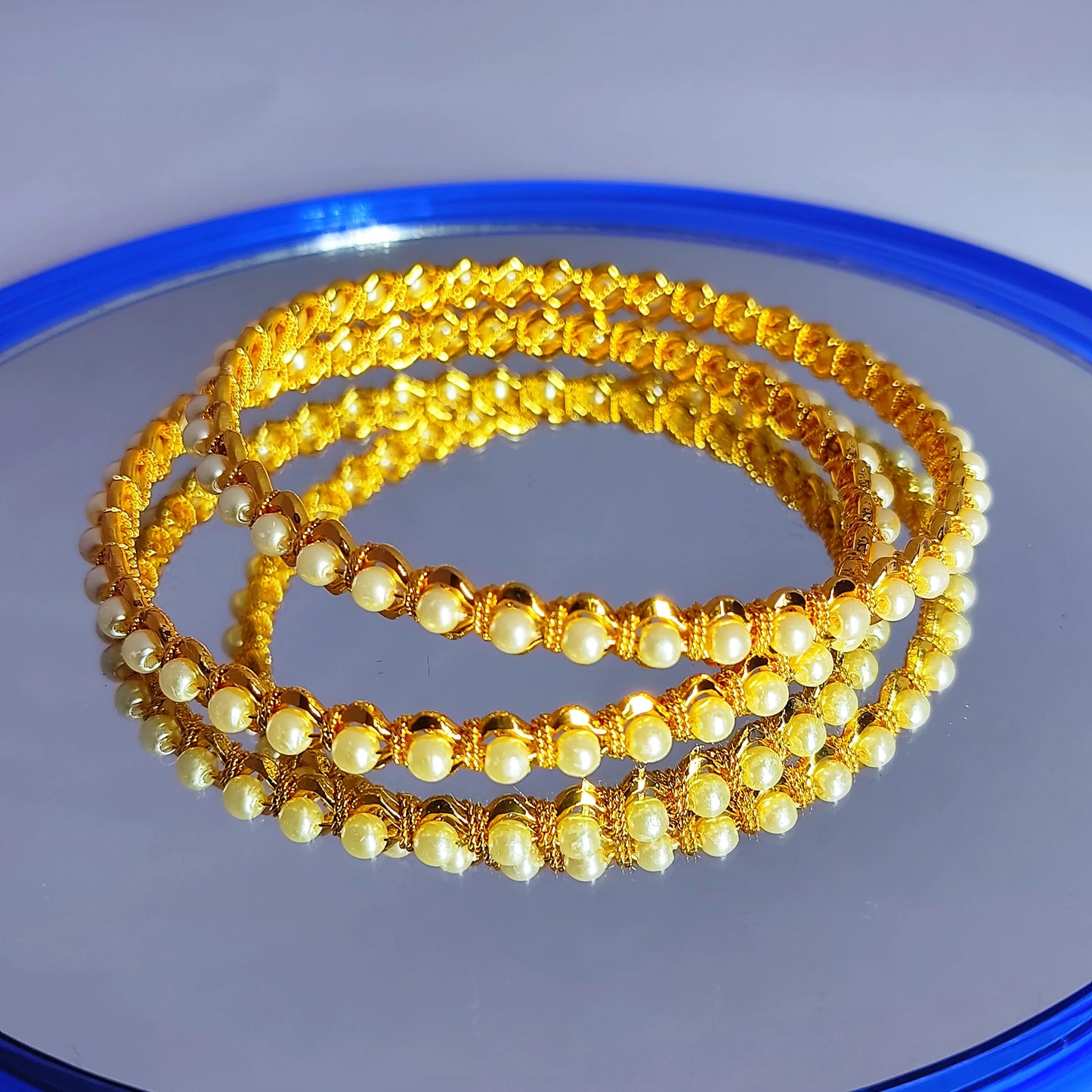 Set of gold plated and pearl beaded bracelets on a reflective surface