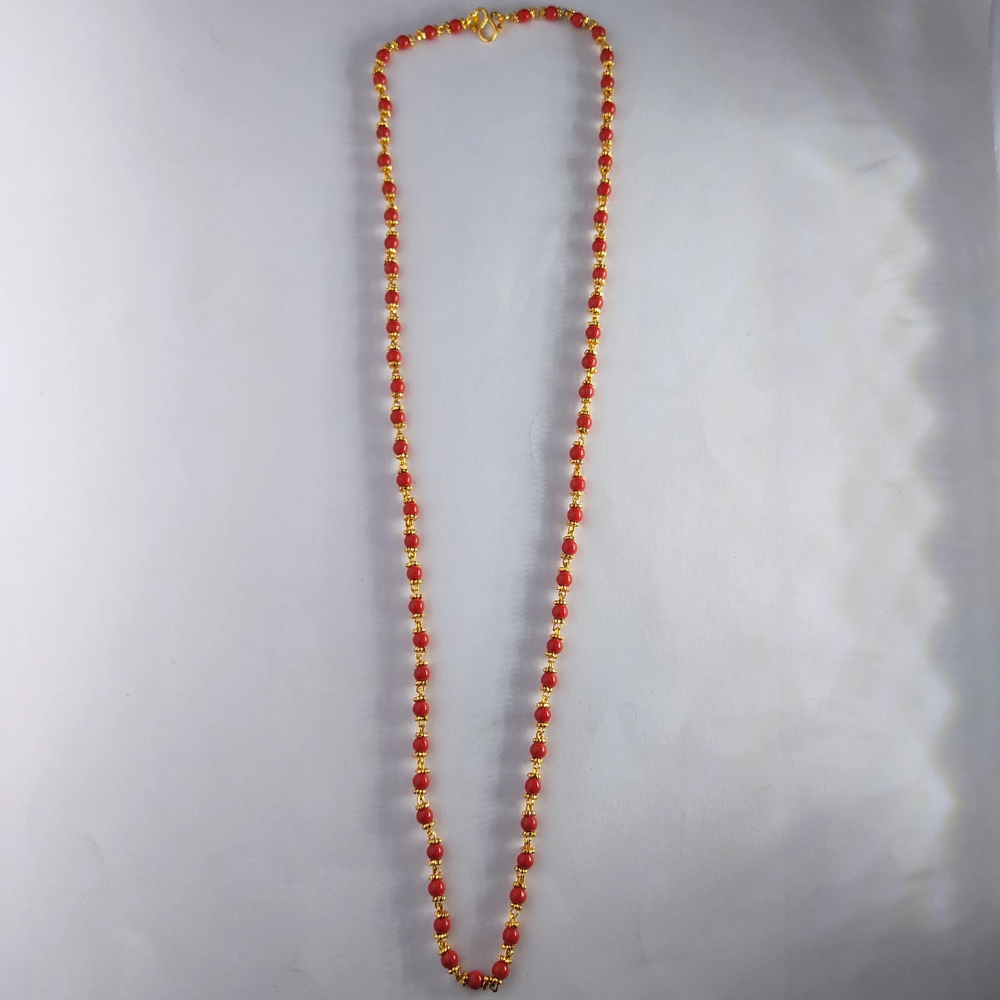 Necklace with red pavizham on a light gray background