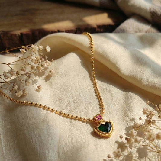 Gold plated necklace with a green palakka pendant on a beige fabric background