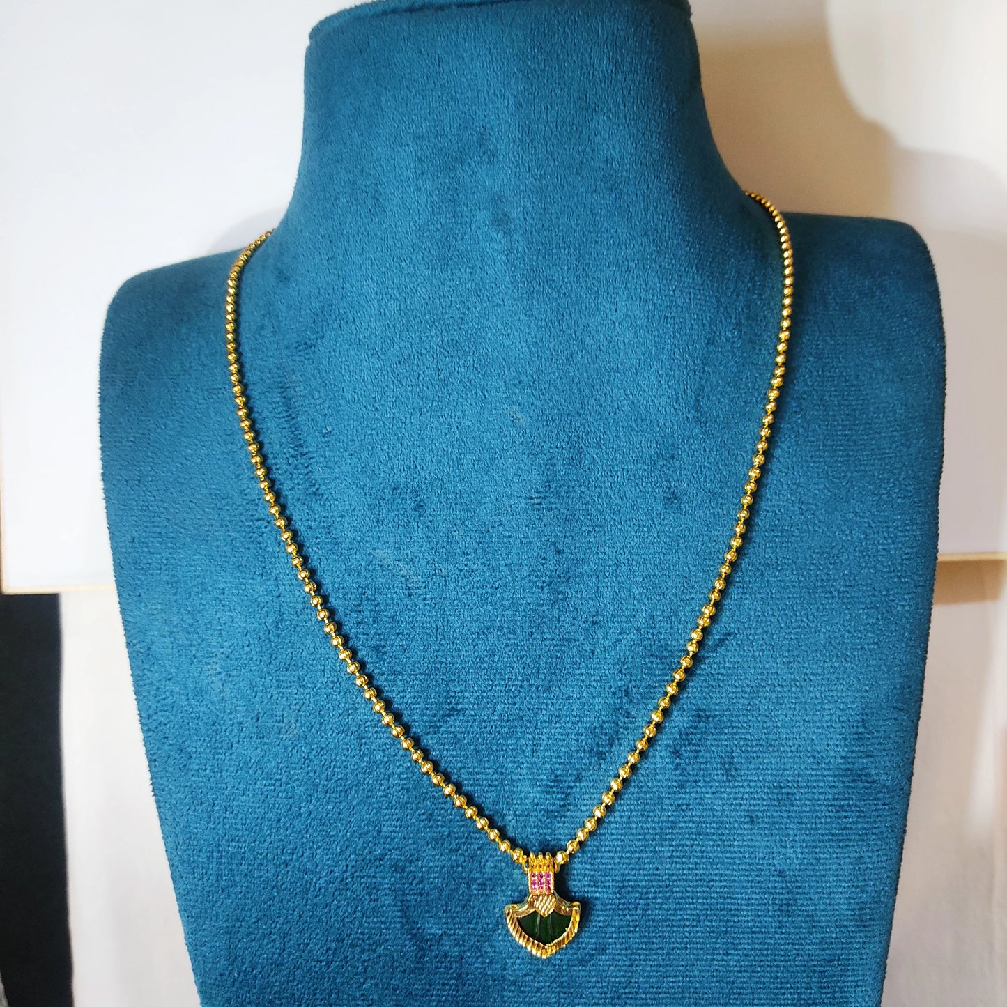 Gold plated necklace with a green palakka on a blue mannequin