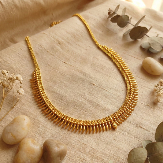 Gold plated necklace on a textured surface with stones and plants