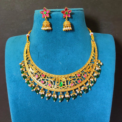Antique gold plated crescent Hasli choker necklace set with intricate openwork, green bead drops, pink stone accents, and matching flower-shaped jhumka earrings on a blue display stand.