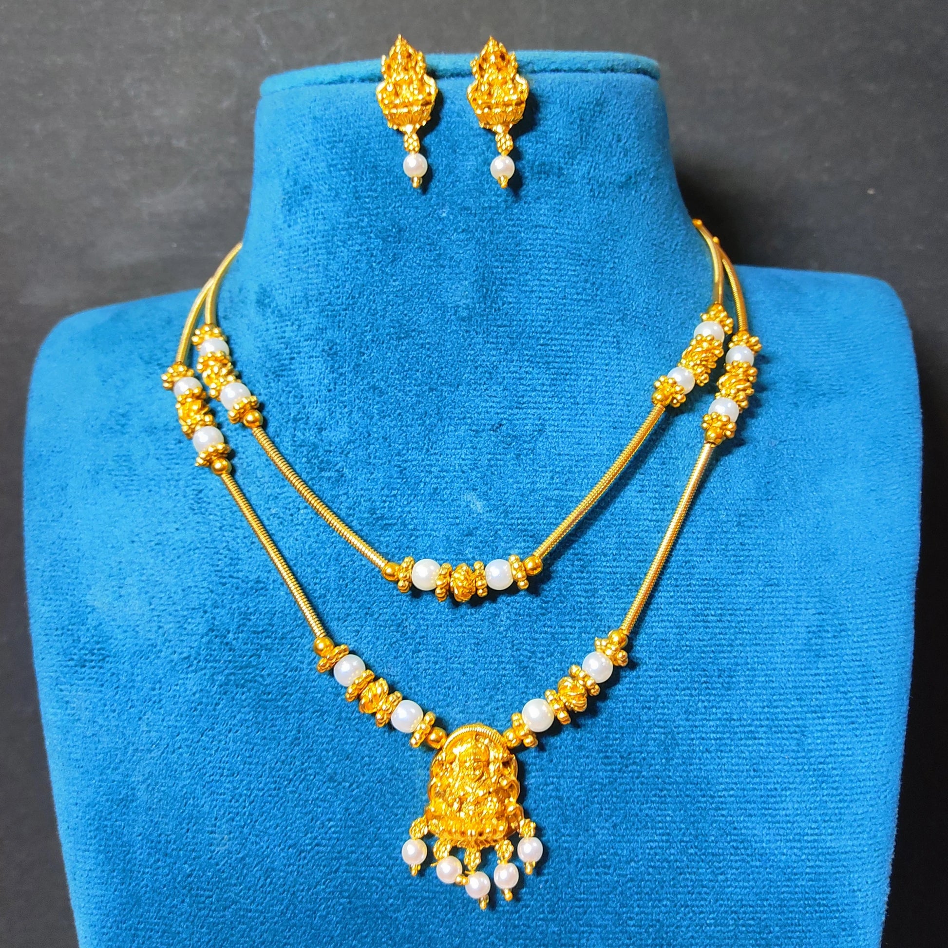 traditional gold-plated double-layer necklace set with a Goddess Laxmi pendant and white pearls displayed on a vibrant blue velvet mannequin bust, including matching Laxmi drop earrings.