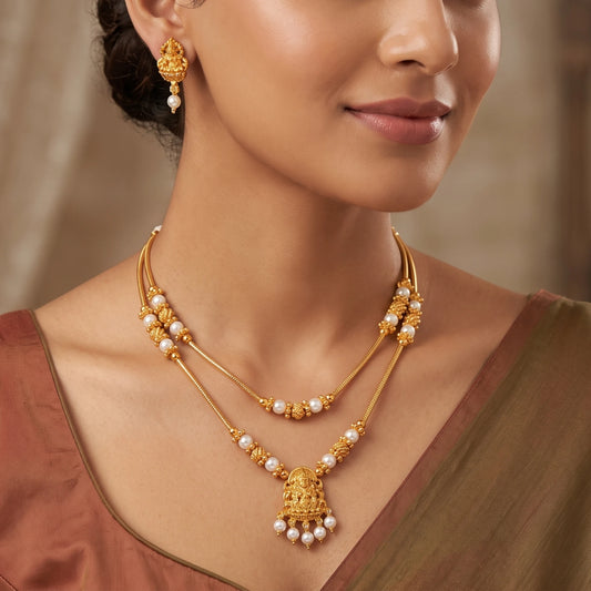 Model wearing a traditional gold-plated double-layer necklace set with a Goddess Laxmi pendant and white pearls, including matching Laxmi drop earrings.
