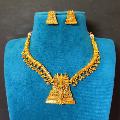 The necklace features a curved, rigid gold toned collar band adorned with a delicate fringe of dangling micro-gold beads, anchored by a prominent, tiered temple gopuram tower pendant intricately engraved with a divine deity figure.