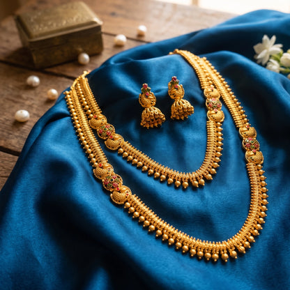 Antique gold plated temple jewelry set featuring a long haram necklace, a matching short choker necklace, and bell-shaped jhumka earrings with traditional South Indian spiked golden bead and floral design