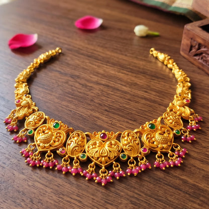 A traditional South Indian Guttapusalu-style short choker necklace and matching drop earrings in a matte antique gold finish on a table shot