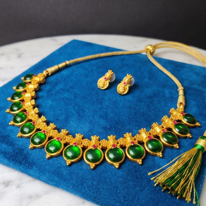 Antique Gold-tone necklace and matching stud earrings with large green enamel coated pendants and small red accent stones, displayed on a blue velvet surface.