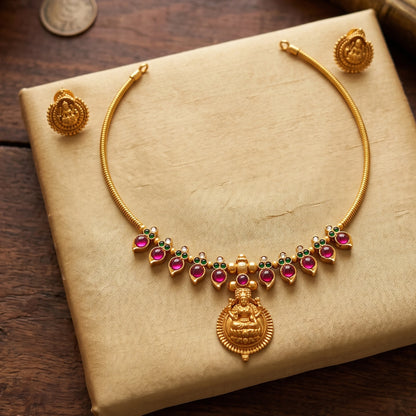 matte antique gold finish Hasli choker necklace featuring alternating pink and green cabochon stones and a central Goddess Lakshmi pendant with matching earrings.