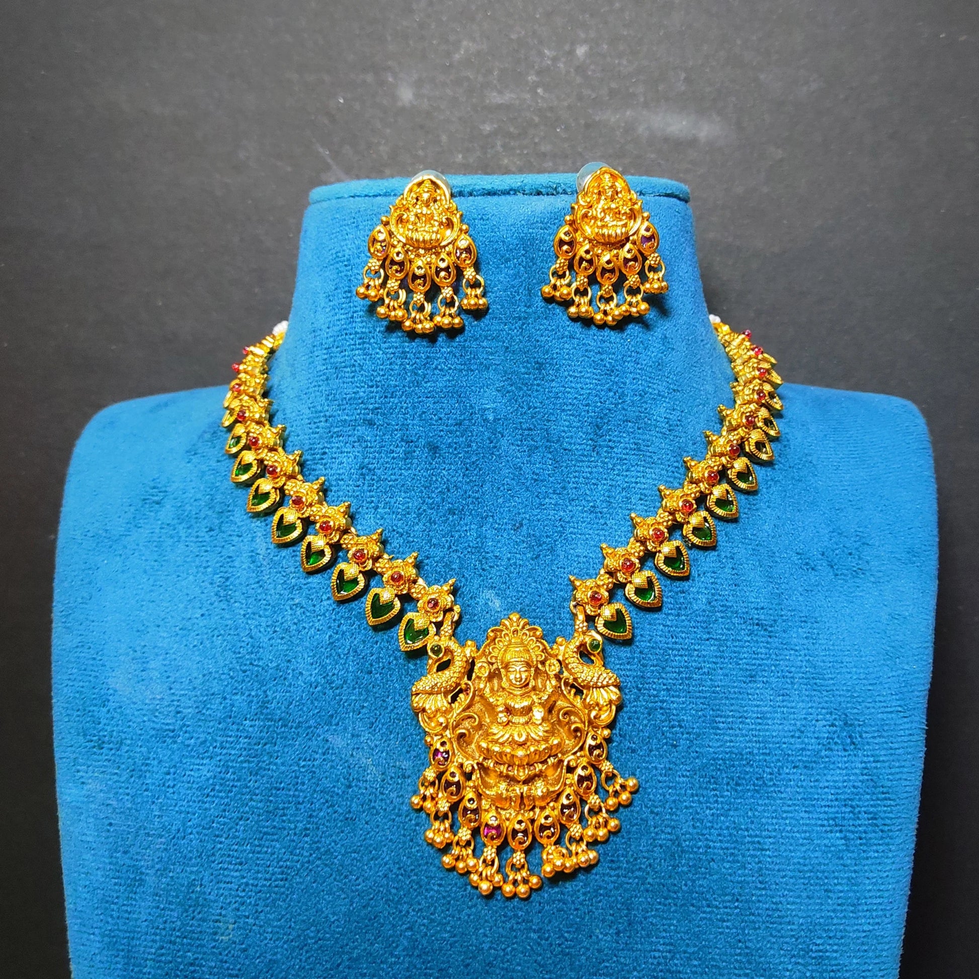 Gold-toned traditional necklace and matching earrings displayed on a blue jewelry bust against a dark gray background.