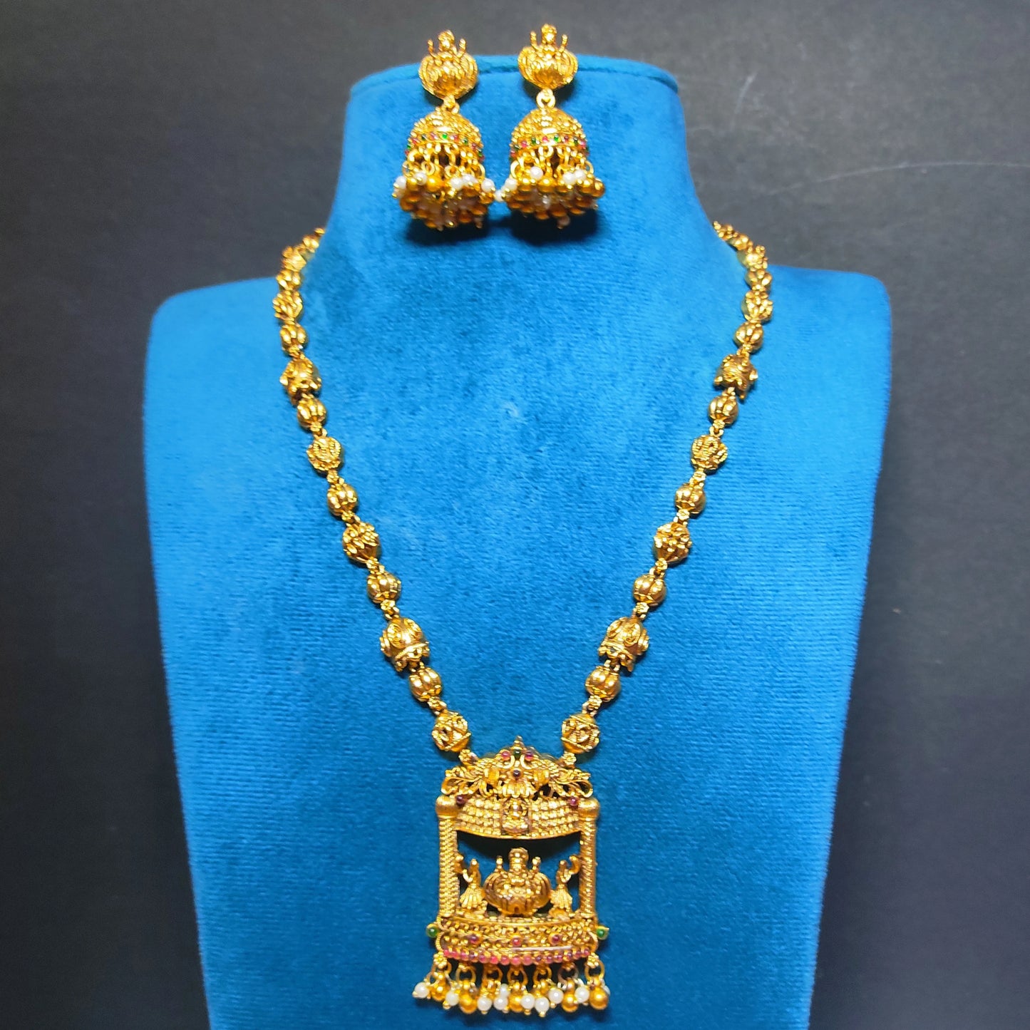 antique gold finish lakshmi pendant haram with matching earrings on a blue mannequin