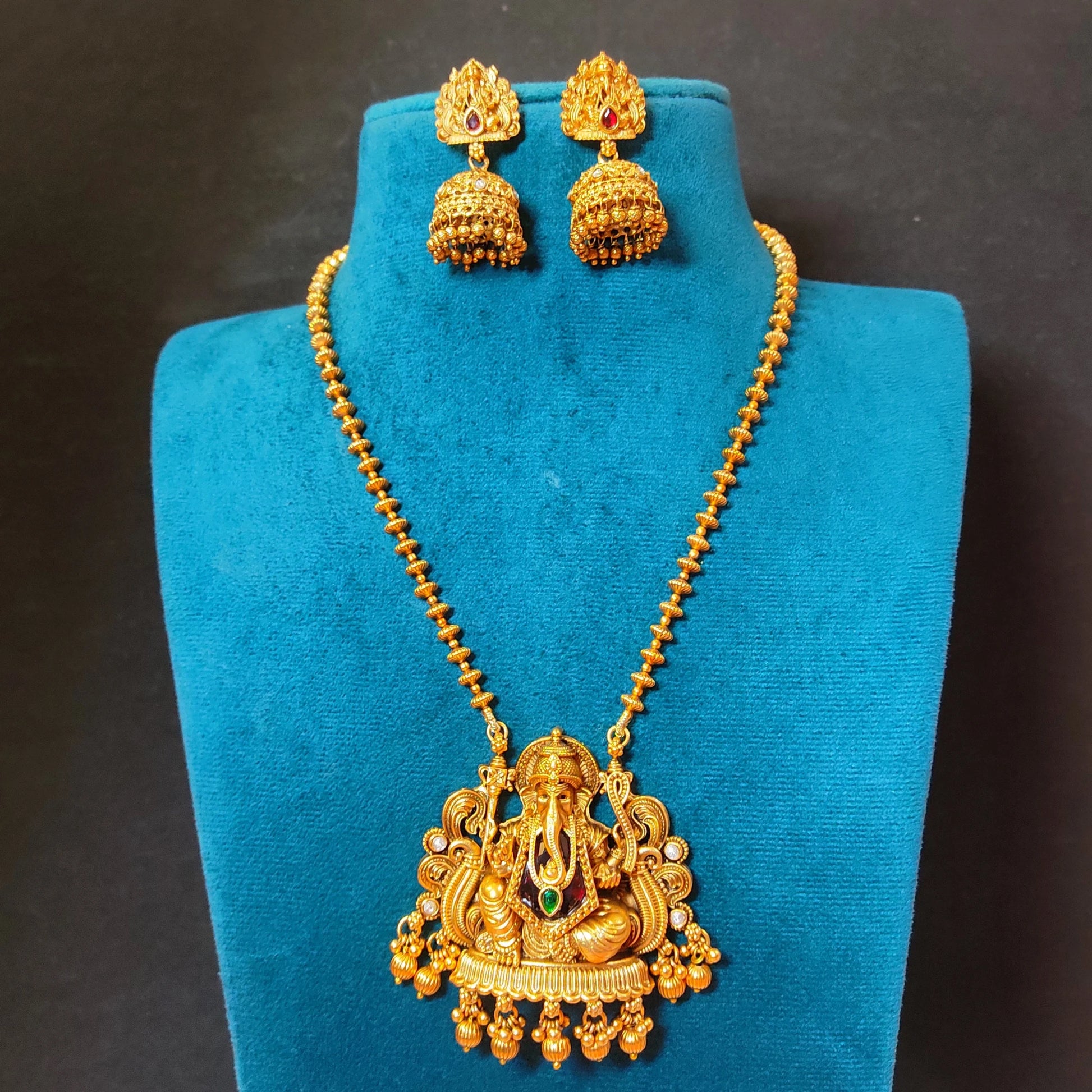 Traditional Indian matte antique gold temple necklace featuring a Lord Ganesha pendant and matching Jhumka earrings on a blue mannequin