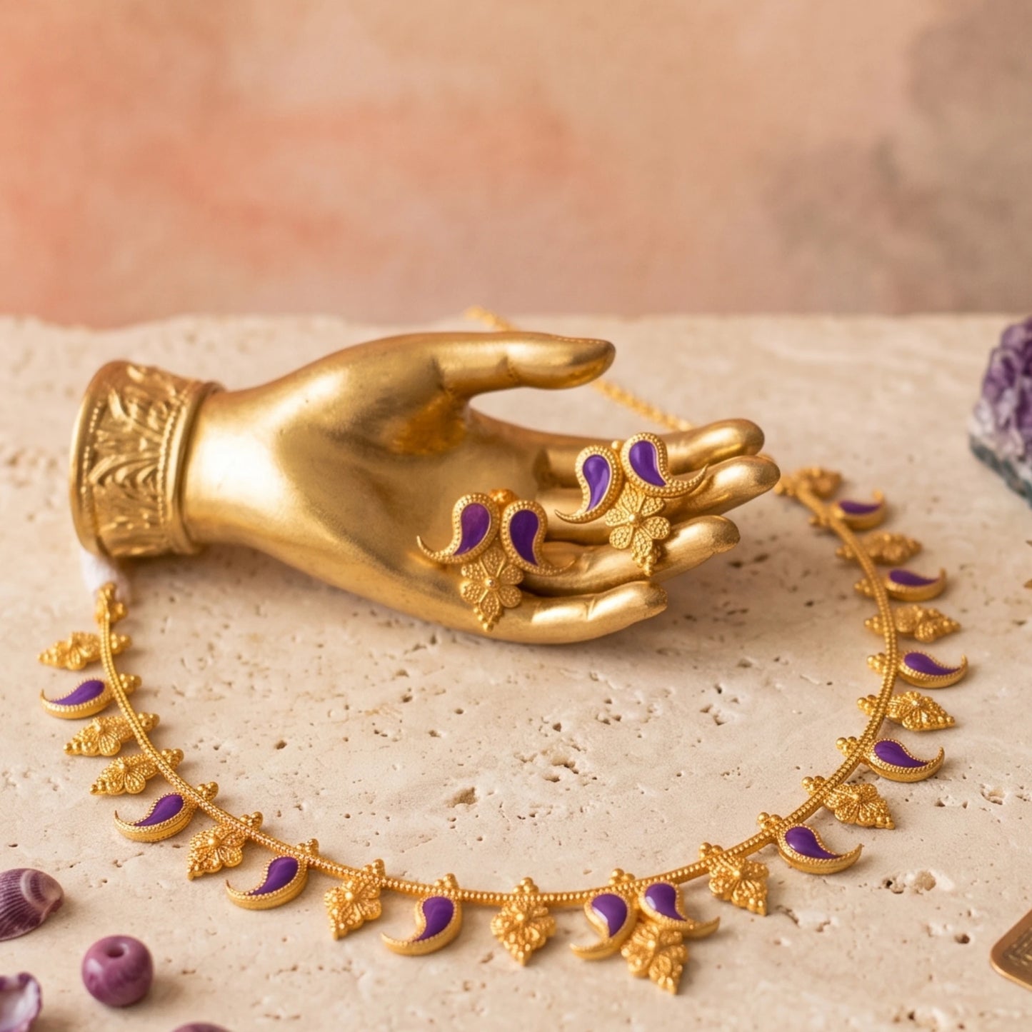 Gold-toned jewelry set displayed on a beige stone surface, including a necklace with crescent and floral motifs and matching earring, both accented with purple enamel, shown with a gold toned mannequin hand.