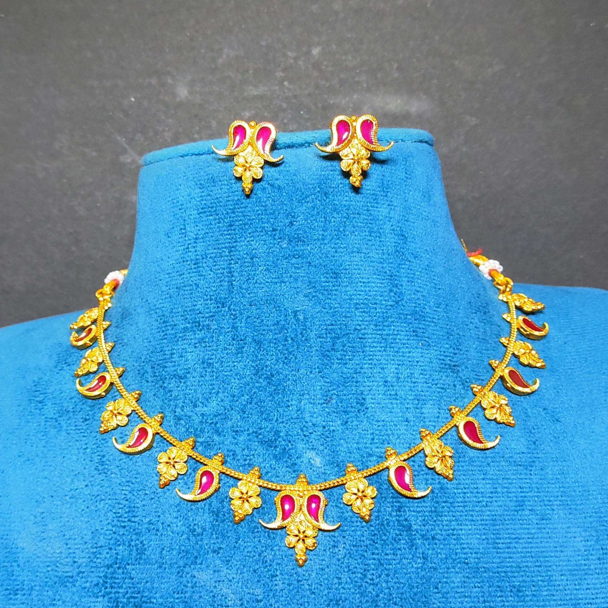 Gold-toned traditional jewelry set featuring a necklace and matching earrings with pink/lavender enamel accents, displayed on a blue velvet jewelry bust against a dark gray background.