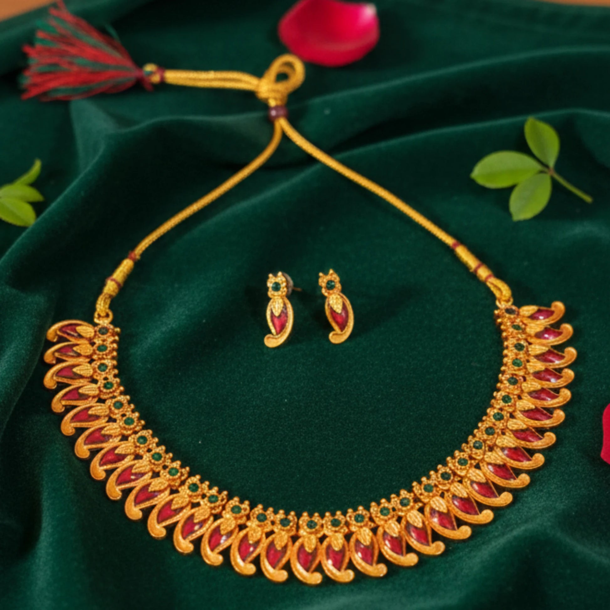 Antique Gold Finish Mango necklace with red and green stones on a green fabric background