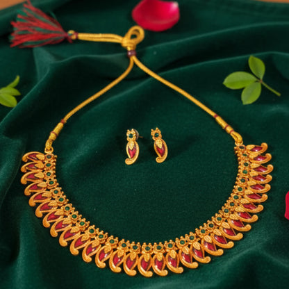 Antique Gold Finish Mango necklace with red and green stones on a green fabric background