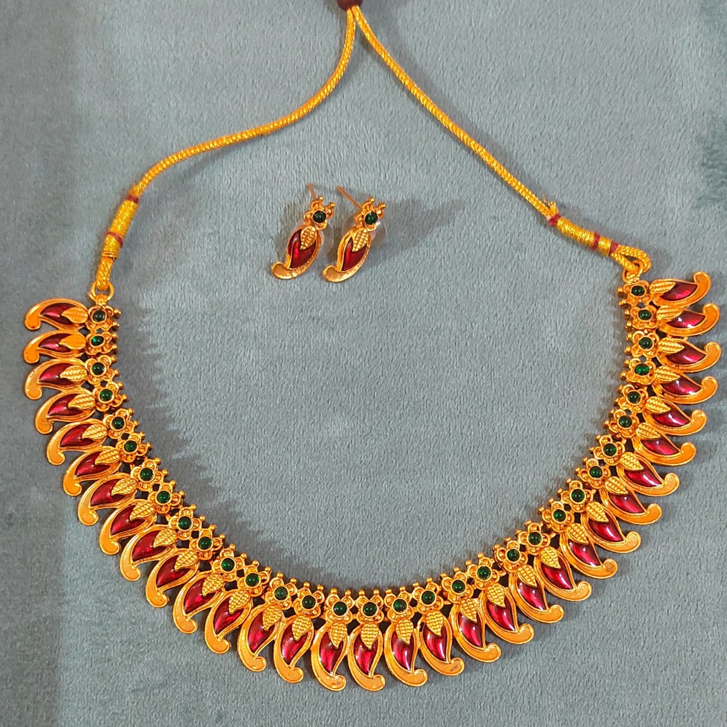 Antique Gold Finish Mango necklace with red and green stones and matching earrings on a gray background