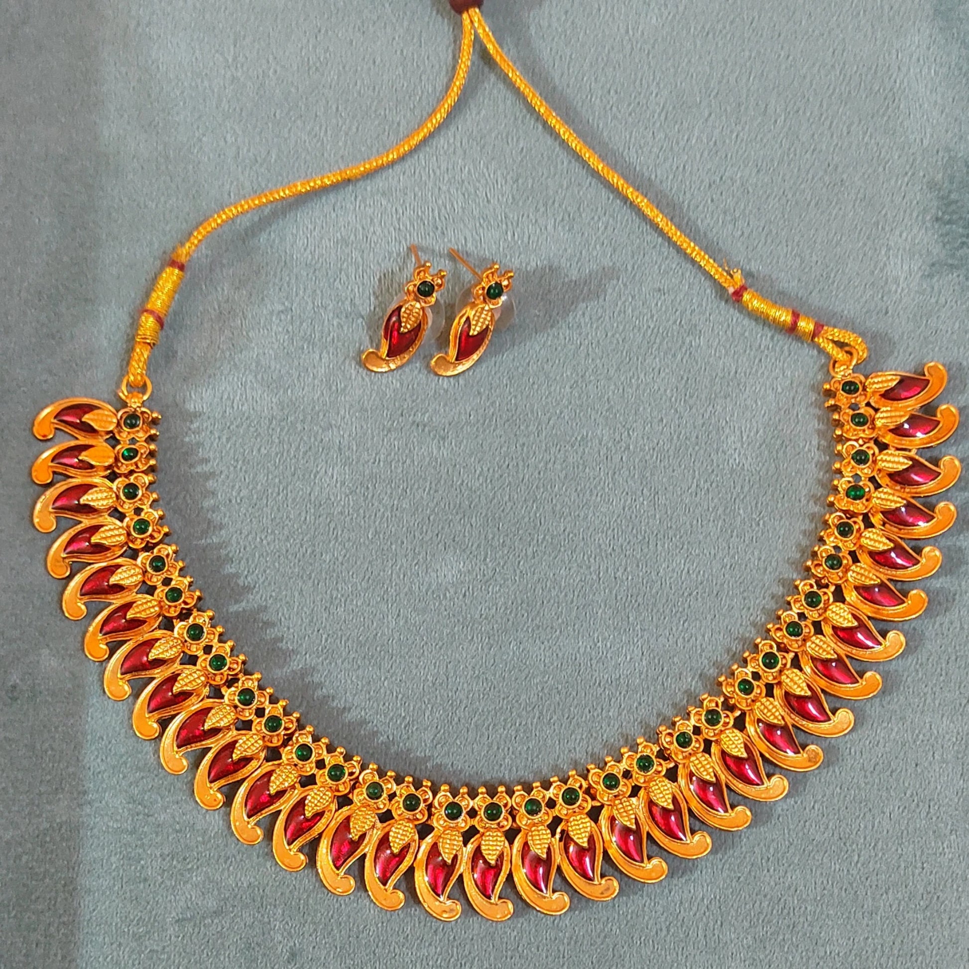 Antique Gold Finish Mango necklace with red and green stones and matching earrings on a gray background